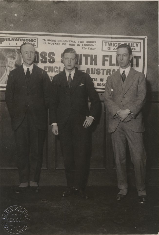 Ross Smith (left) and Keith Smith (right) with Edward Prince of Wales (centre) after presenting a lecture on their England to Australia flight in London. An advertisement for the lecture can be seen in the background. SLSA: PRG 18/10/6