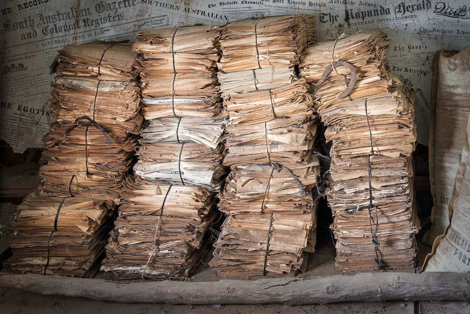 Dispatches, Home and Abroad. Piles of newspapers wrapped in string leaning against a wall.
