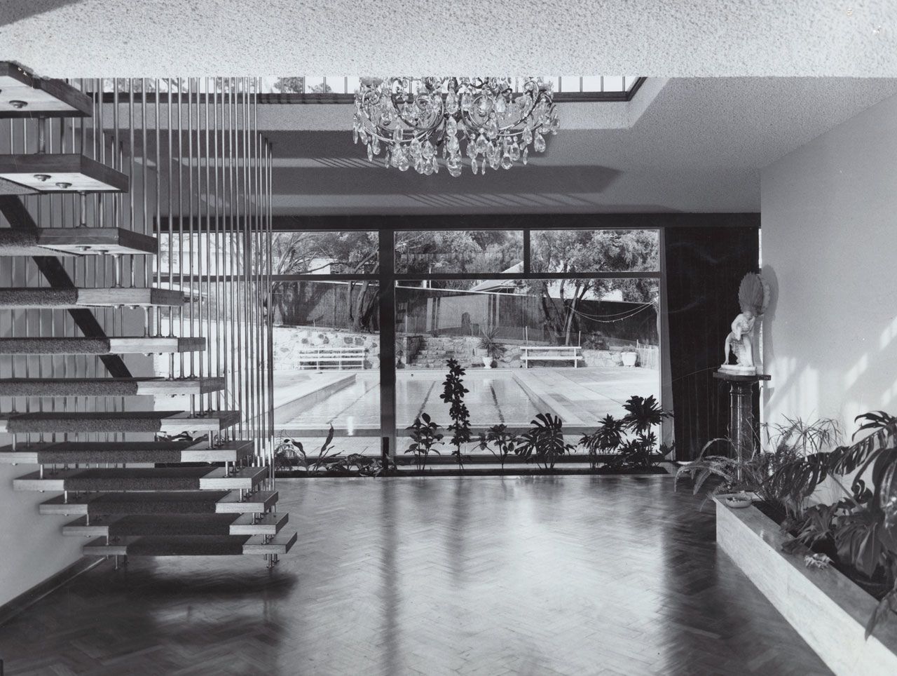Interior view of house on Balfour Road, Springfield, built for Alf Brown and designed by John S. Chappel Pty Ltd, architect. Showing view of room with interior garden, large windows looking out to the swimming pool, and staircase with floating stairs, February 1962. SLSA: BRG 346/29/27/10